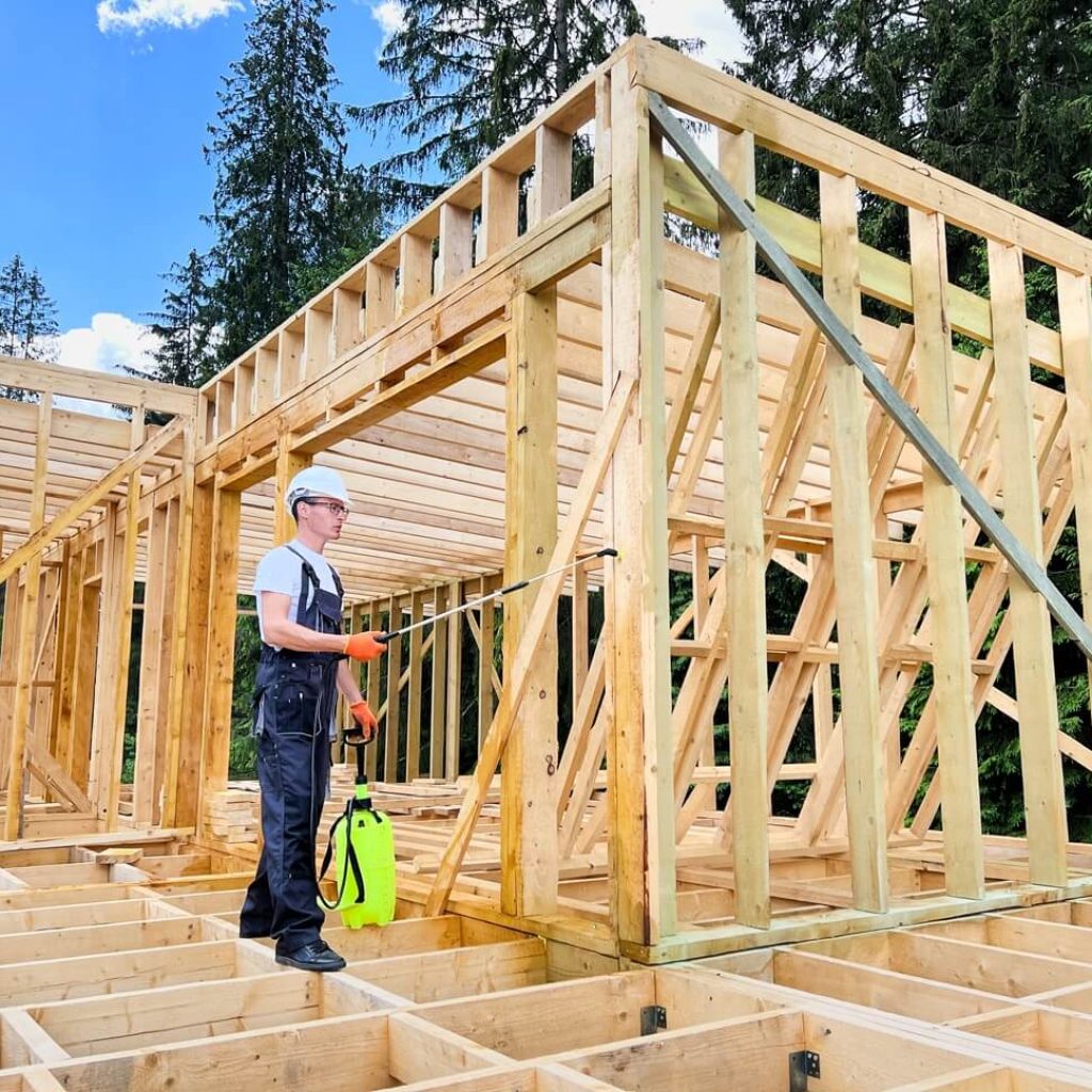 Why Choose Our Team for Tiny Home Building Services​ Construction worker applying moisture control treatment in wooden frame of a tiny home under construction, emphasizing energy efficiency and structural strength in Fredericksburg, Texas.